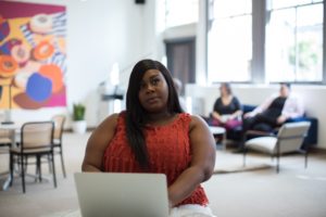 black woman in red shirt sitting in an office with laptop