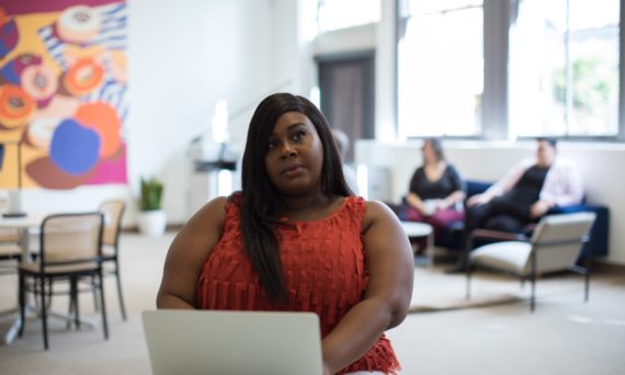 black woman in red shirt sitting in an office with laptop